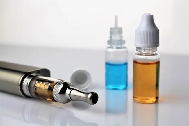 Vape Juice Ingredients. A vape pen and bottles filled with colored liquids representing vaping juice ingredients