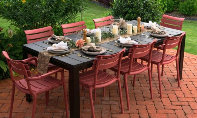 Outdoor dining setup on a brick patio with a dark table and red chairs