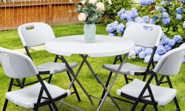 A round table with four white folding chairs on a lawn, surrounded by blooming hydrangeas