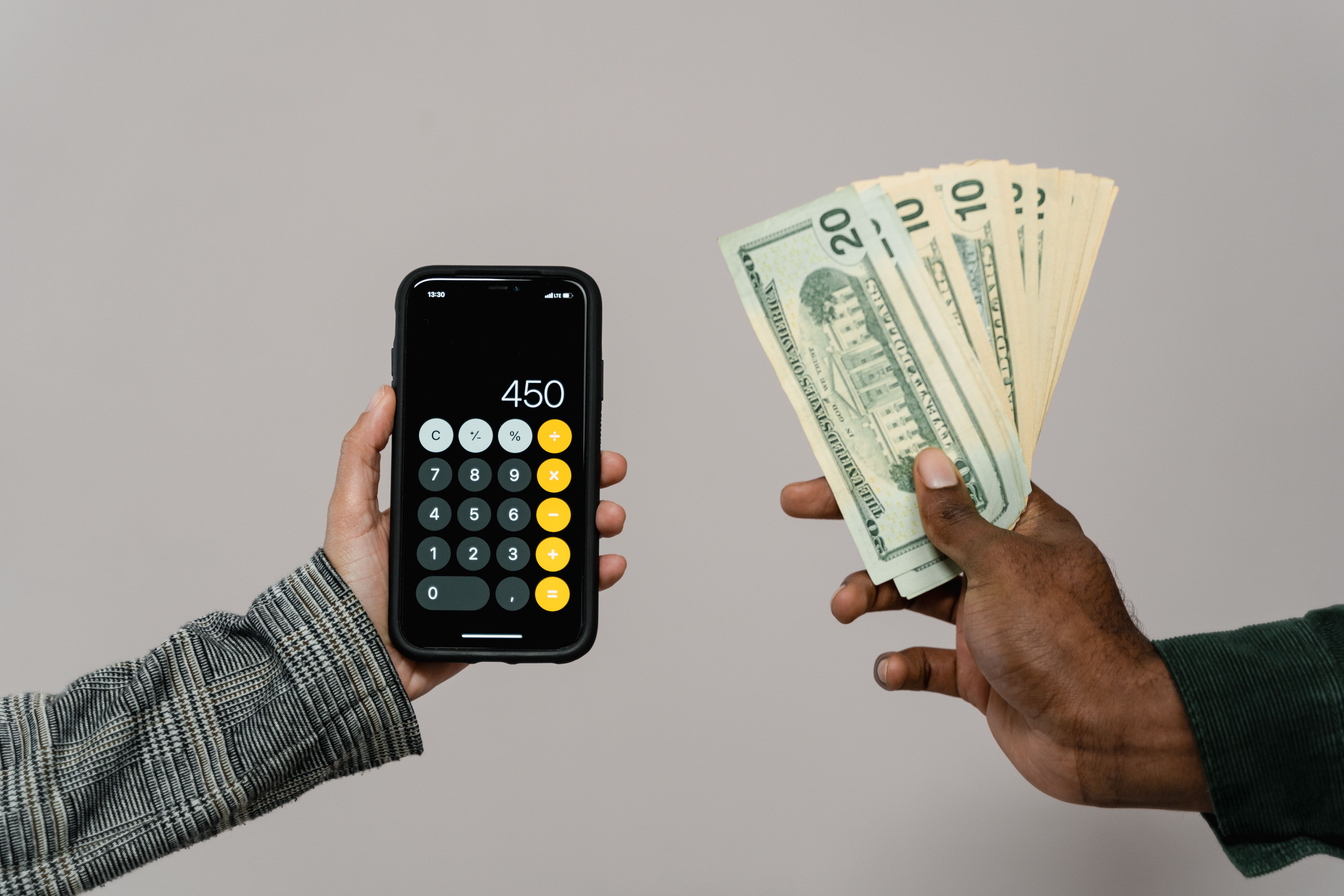 Hands holding cash next to a smartphone showing a payment calculation