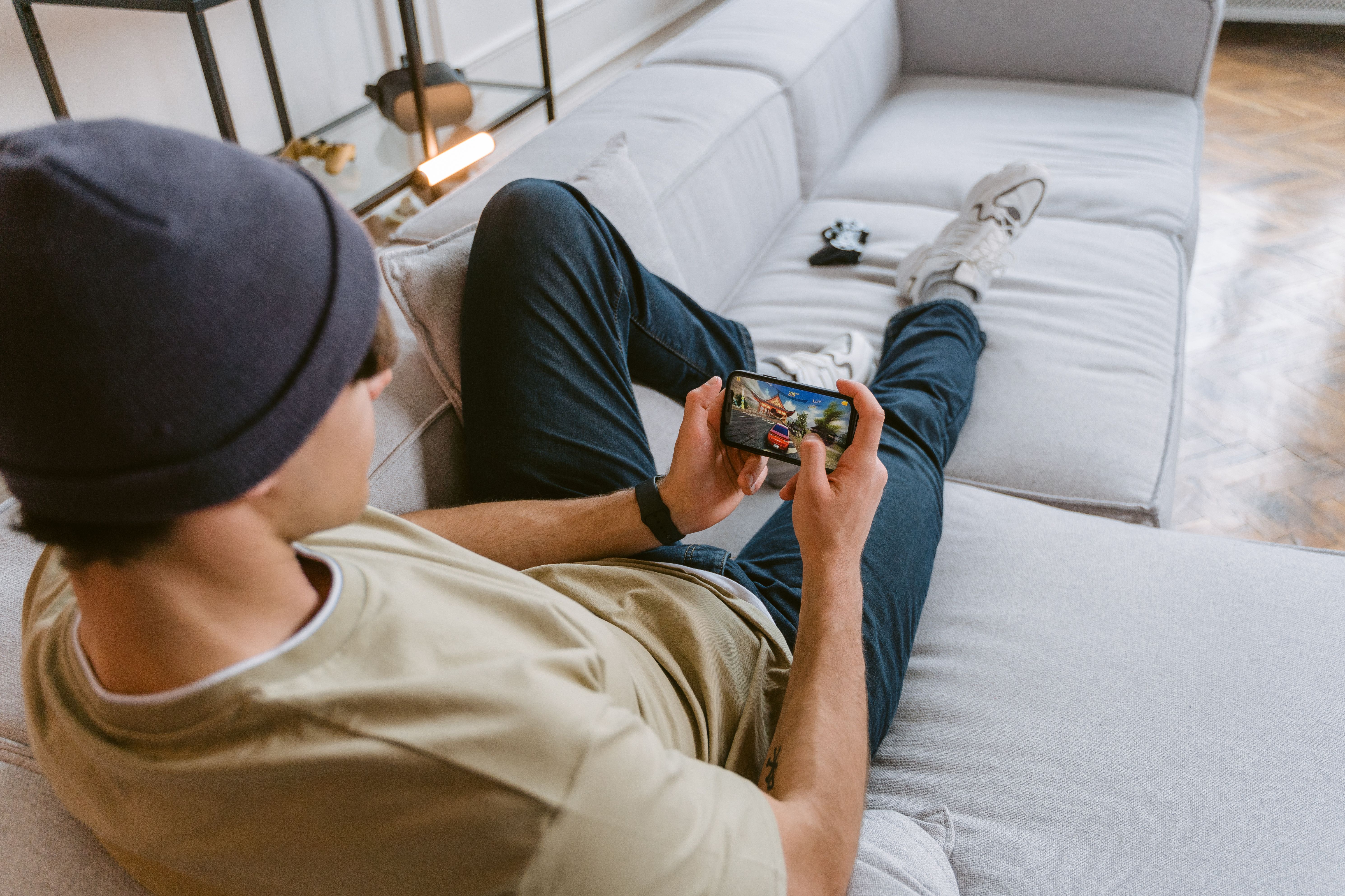 Young man in casual wear playing a mobile game while relaxing on a sofa indoors