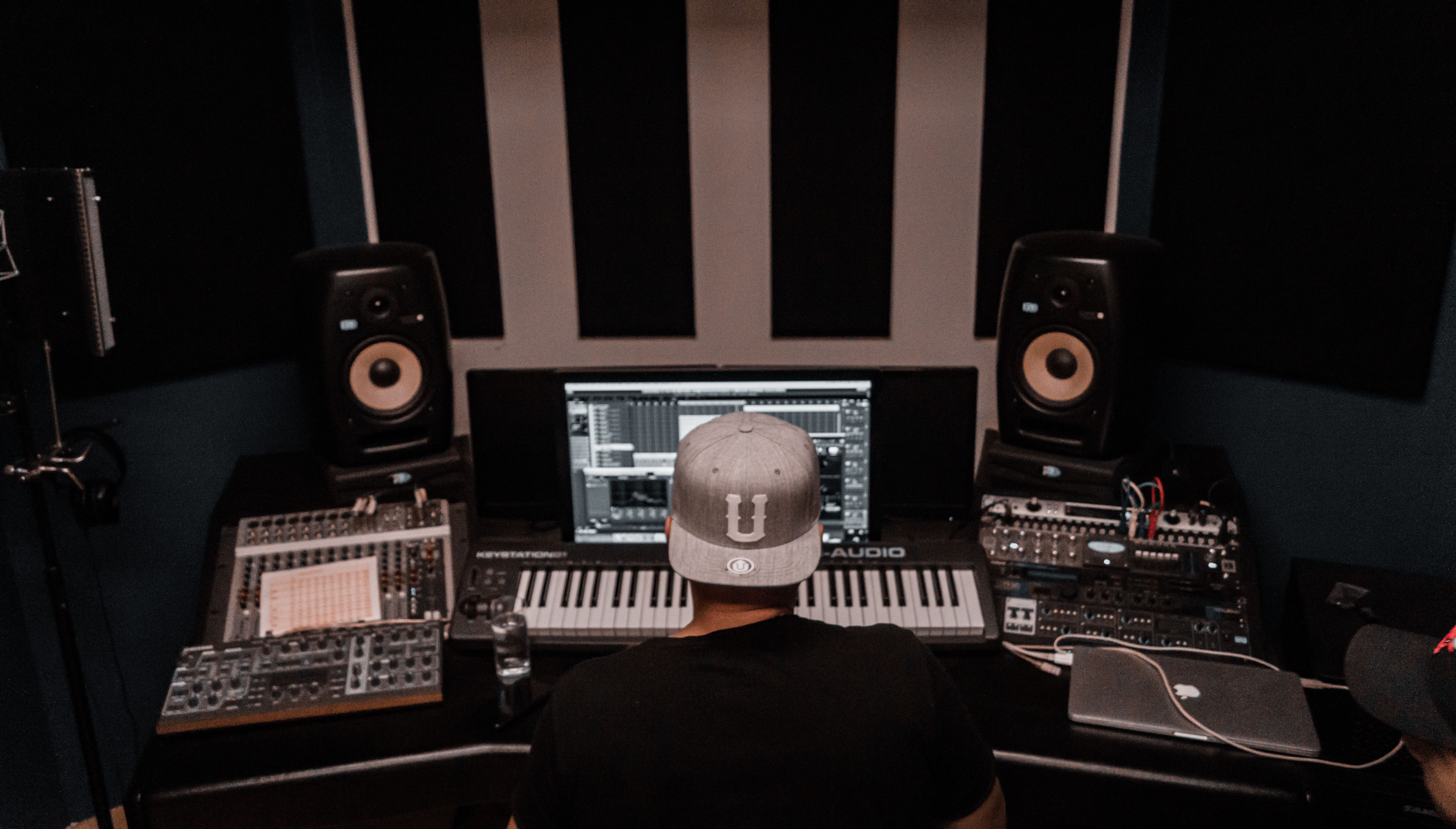 Music producer working among studio keyboards and monitors in a modern recording space.